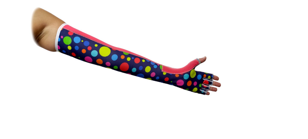 Wyciągnięte ramię ubrane w długi, częściowo palcowy rękaw sięgający od ramienia do końcówek palców, z granatowego materiału w duże, kolorowe kropki i różowym obszyciem, na białym tle.