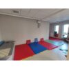 Sala terapii z kolorowymi materacami i sufitowym podnośnikiem przy ścianie