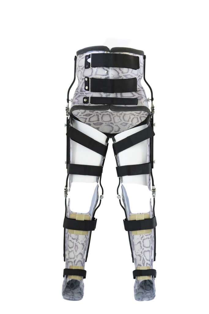 Para ortopedycznych ortez kończyn dolnych obejmujących miednicę, uda, goleń i stopy — plastikowo-metalowa konstrukcja z bocznymi zawiasami, regulowanymi czarnymi paskami i szarawo-białym wzorem przypominającym skórę węża.