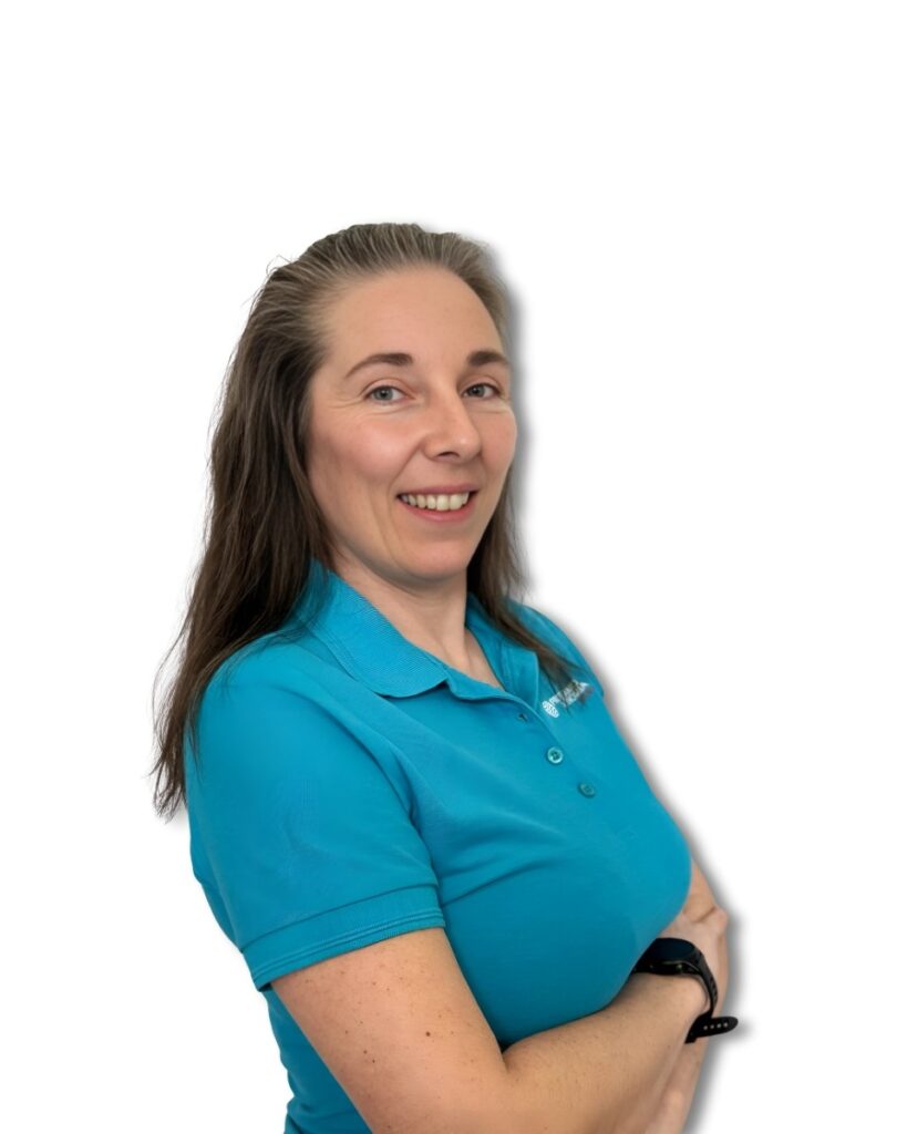 Uśmiechnięta kobieta w turkusowej koszulce polo, stojąca bokiem z założonymi ramionami, długimi brązowymi włosami i czarnym smartwatchem na nadgarstku na białym tle.