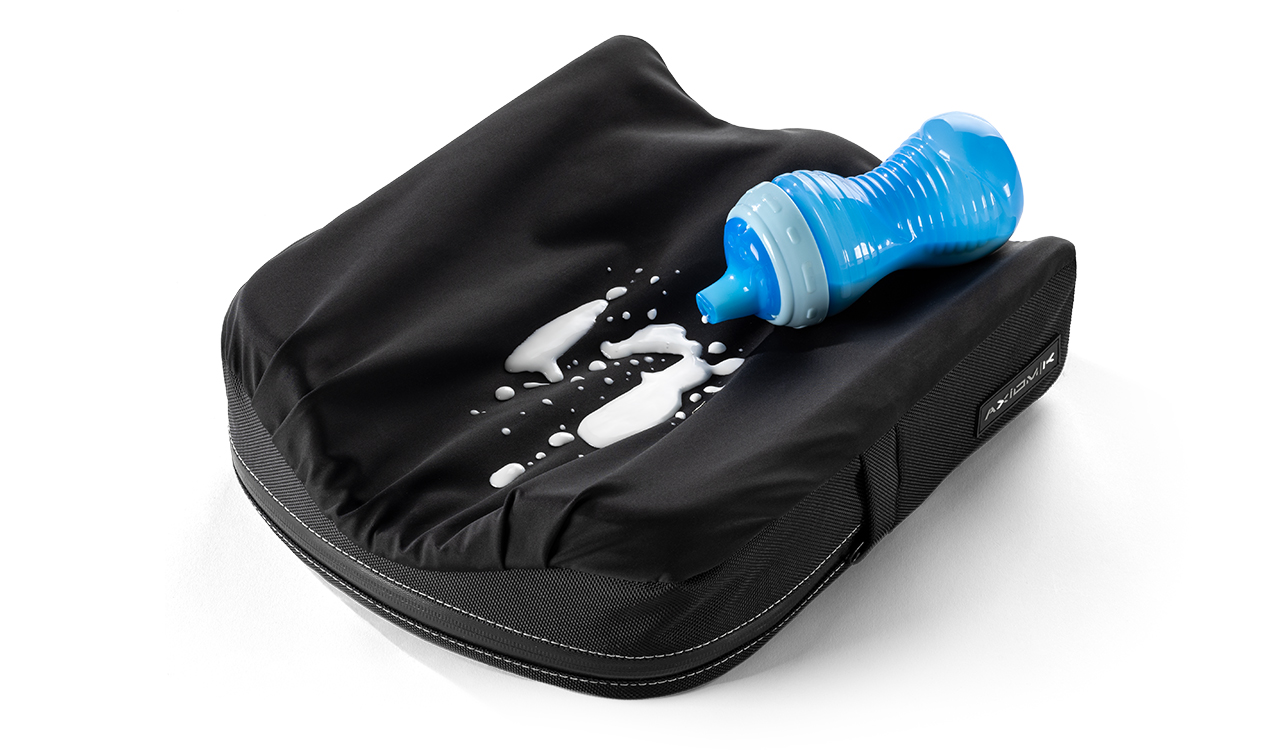 Czarny wodoodporny pokrowiec z rozlanym białym płynem i niebieską butelką dla niemowląt leżącą na wierzchu.