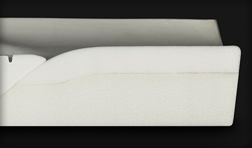 Biały przekrój pianki z zaokrąglonym górnym profilem i cienką żółtą linią przebarwienia na czarnym tle.