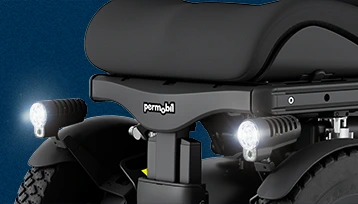 Tylny fragment wózka inwalidzkiego Permobil z siedziskiem, dwoma świecącymi LED-ami i oponami.