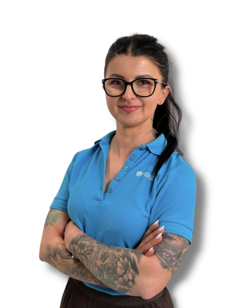 Kobieta z ciemnymi włosami i okularami w niebieskiej koszulce polo, uśmiechnięta, z tatuażami na przedramionach i skrzyżowanymi ramionami.
