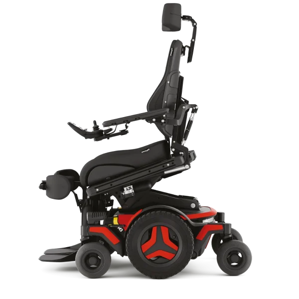 Elektryczny wózek inwalidzki w profilu, czarny z czerwonymi akcentami, regulowane siedzisko i zagłówek oraz joystick na podłokietniku.